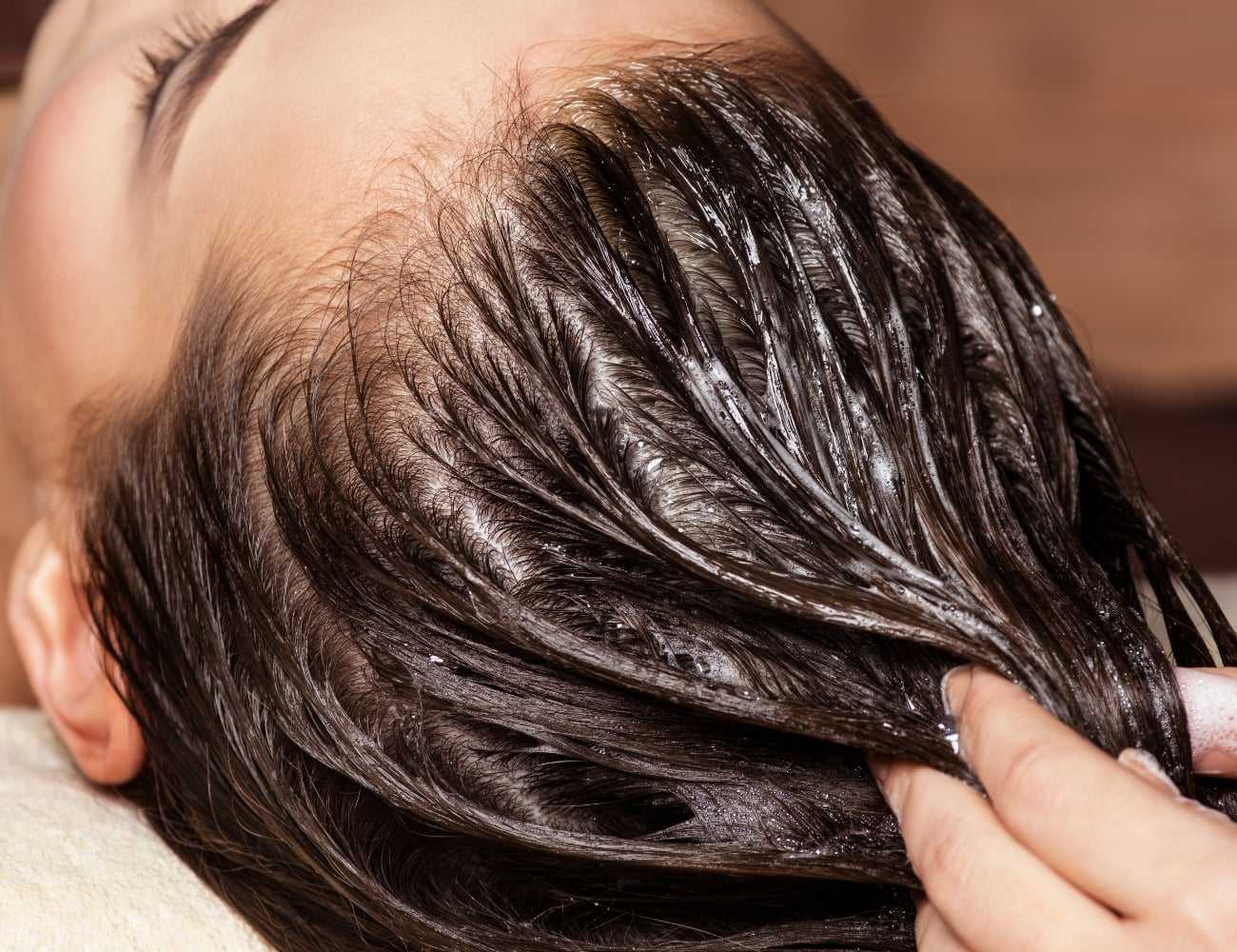 Person receiving a hair treatment with oil being massaged into the scalp.