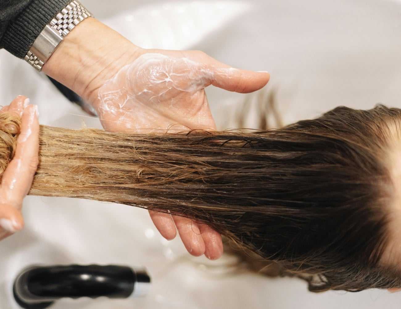 Person receiving a hair treatment, with conditioner applied, in a salon sink.