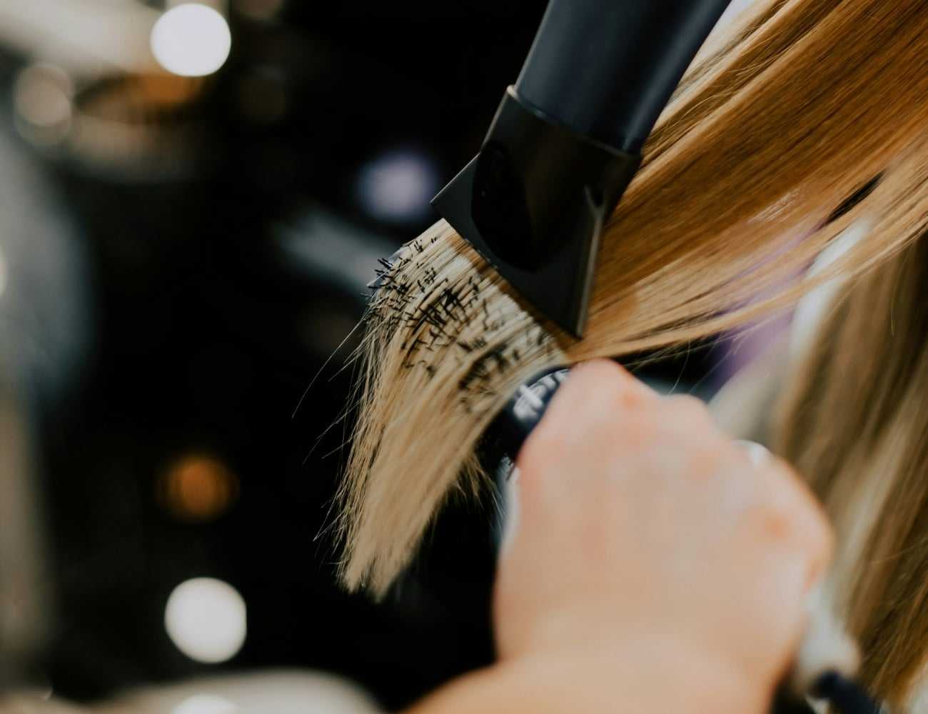 Close-up of a person blow-drying long blonde hair, using a round brush for styling.