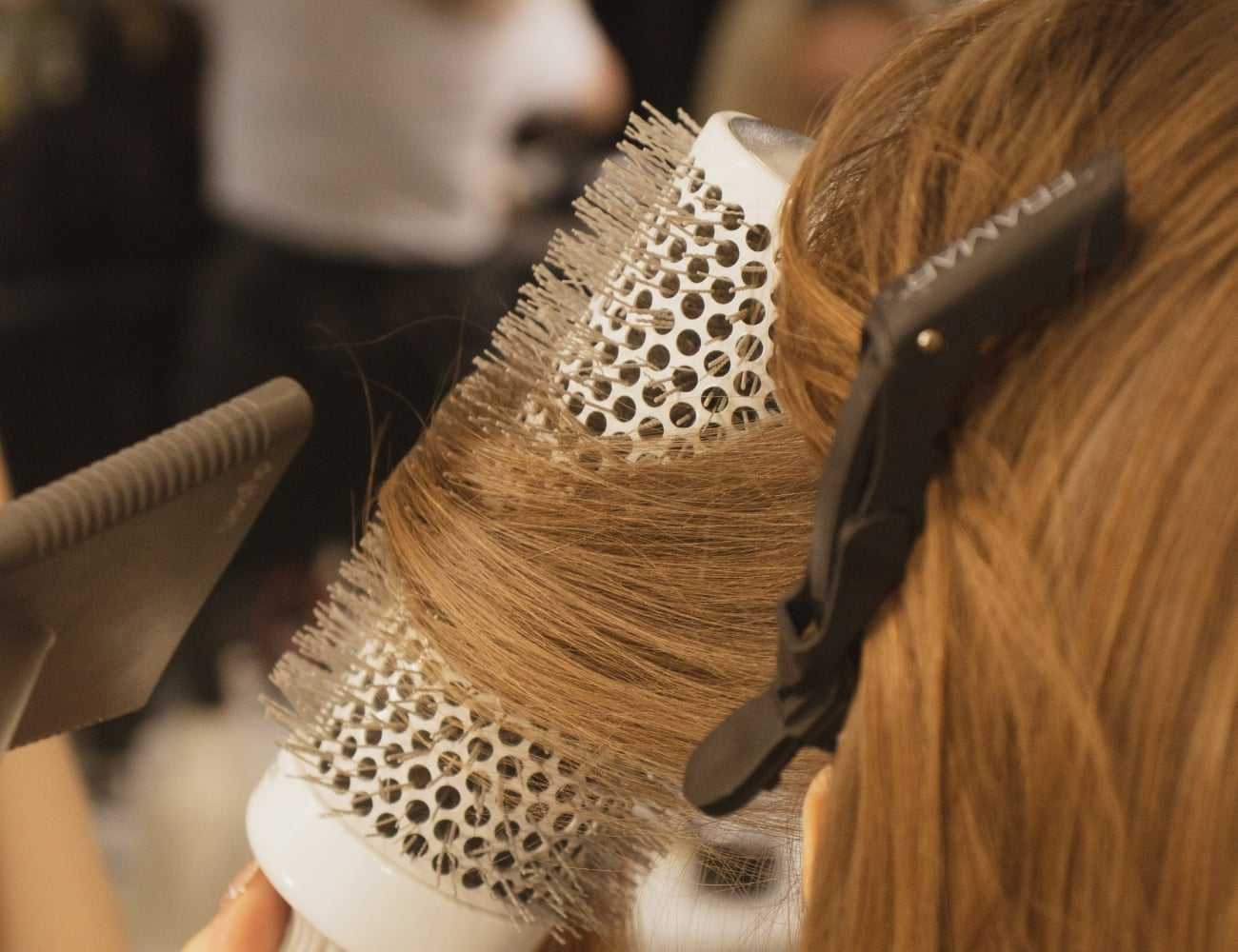 Hair being styled with a round brush and blow dryer in a salon setting.